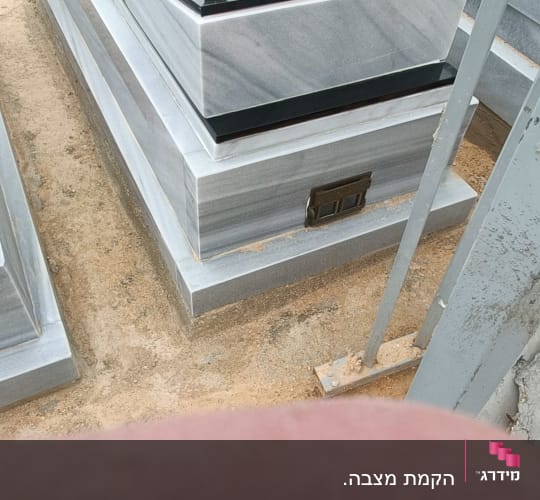 מצבות שיש עם כיתוב ואבנים קטנות מונחות עליהן